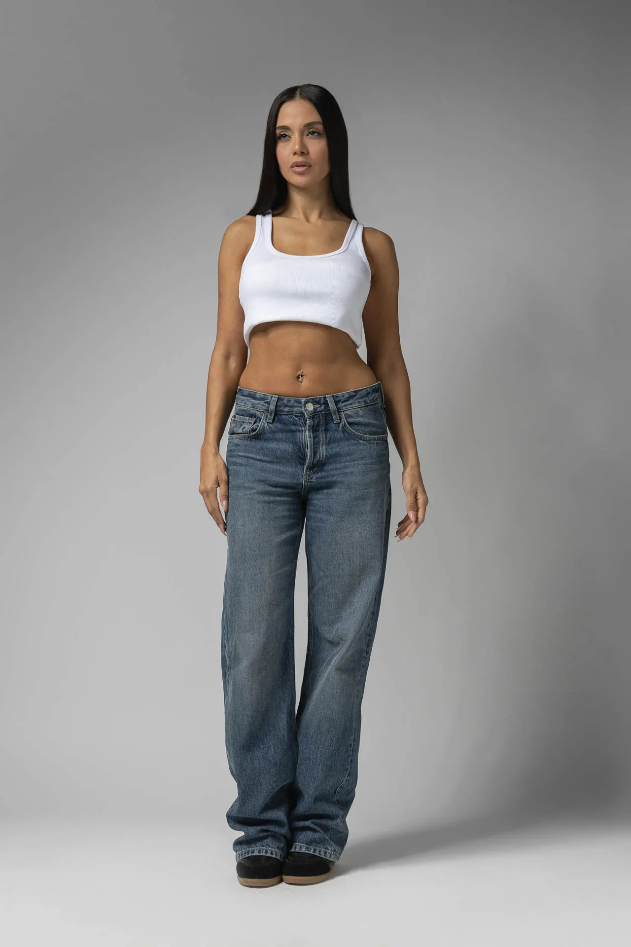 Female model in white cropped tank and blue jeans, gray studio backdrop — Dubai modeling portfolio digitals