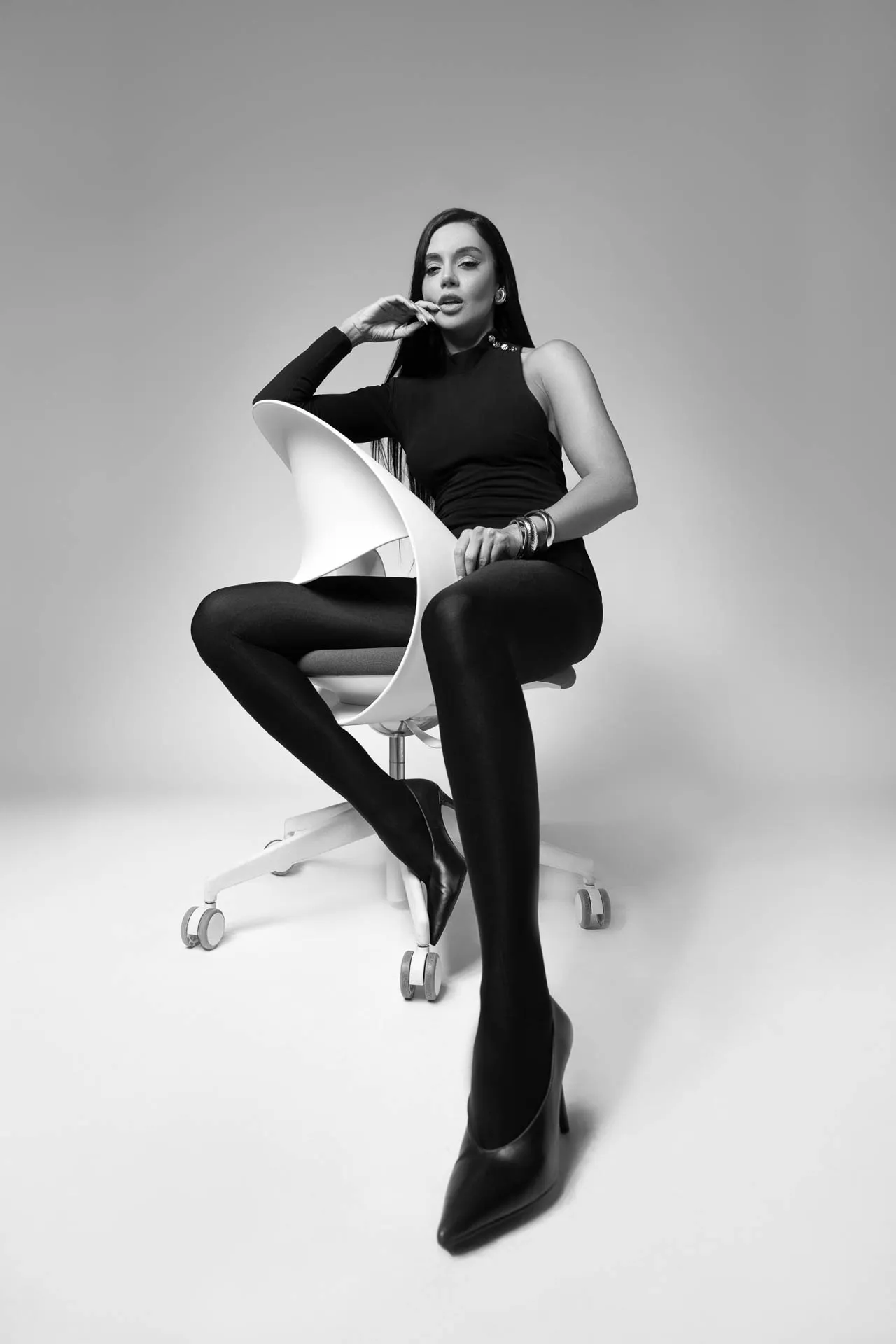 Female model in black seated on a white designer chair, legs crossed — editorial modeling portfolio Dubai