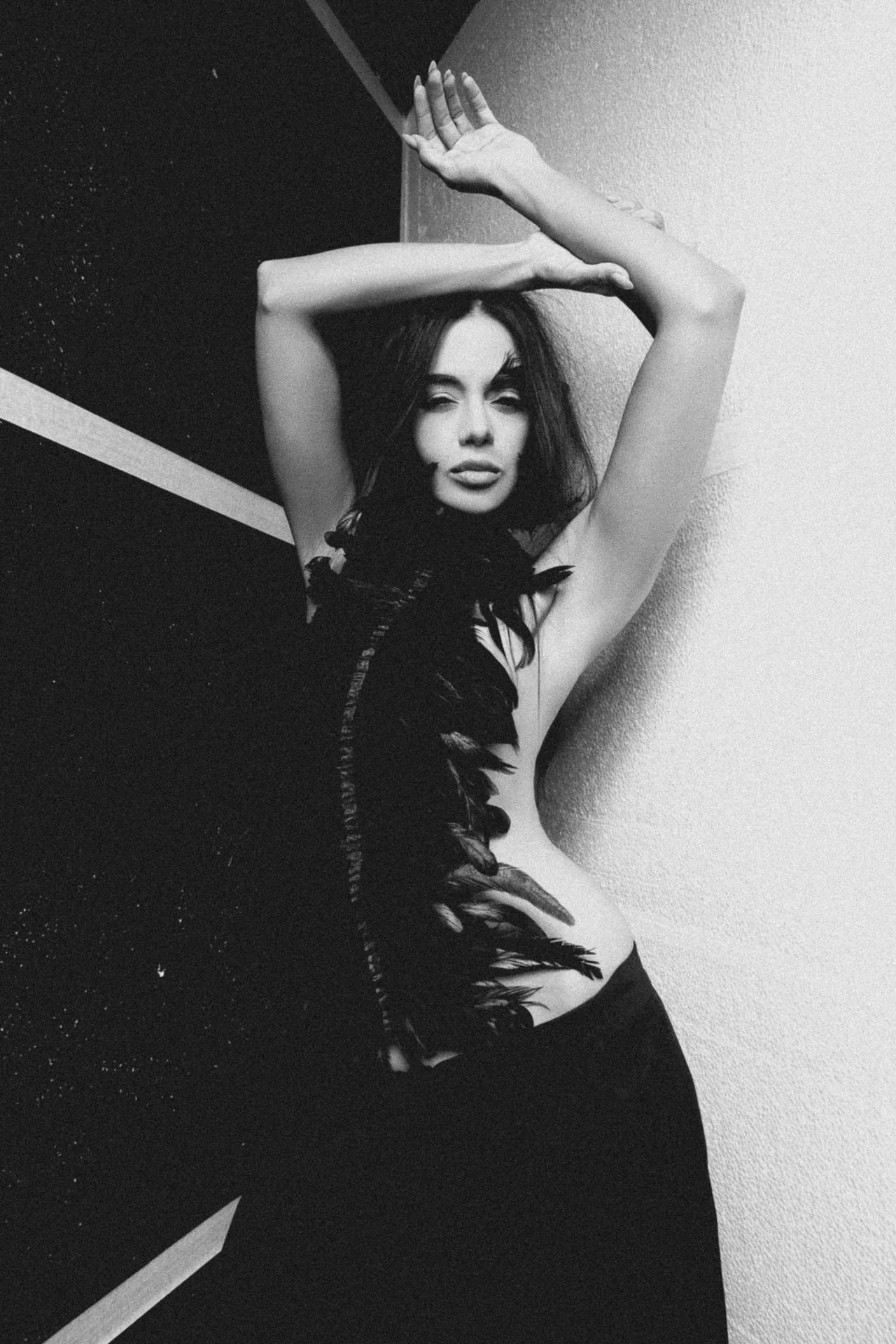 Black-and-white portrait of a woman with arms raised above her head, wearing a feathered garment along her torso.