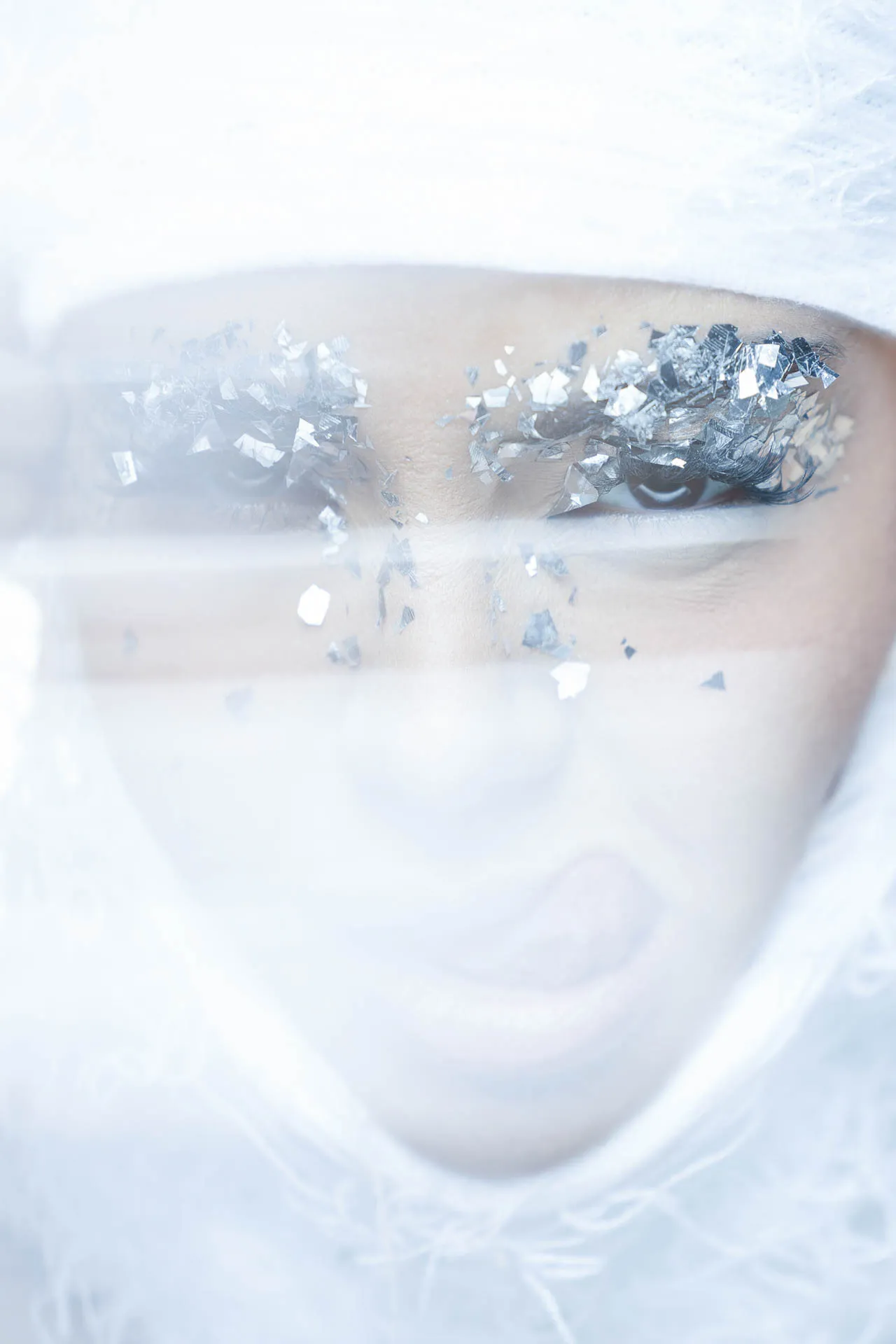 Close-up of an eye with silver foil fragments scattered on the lashes for an icy, artistic makeup look.