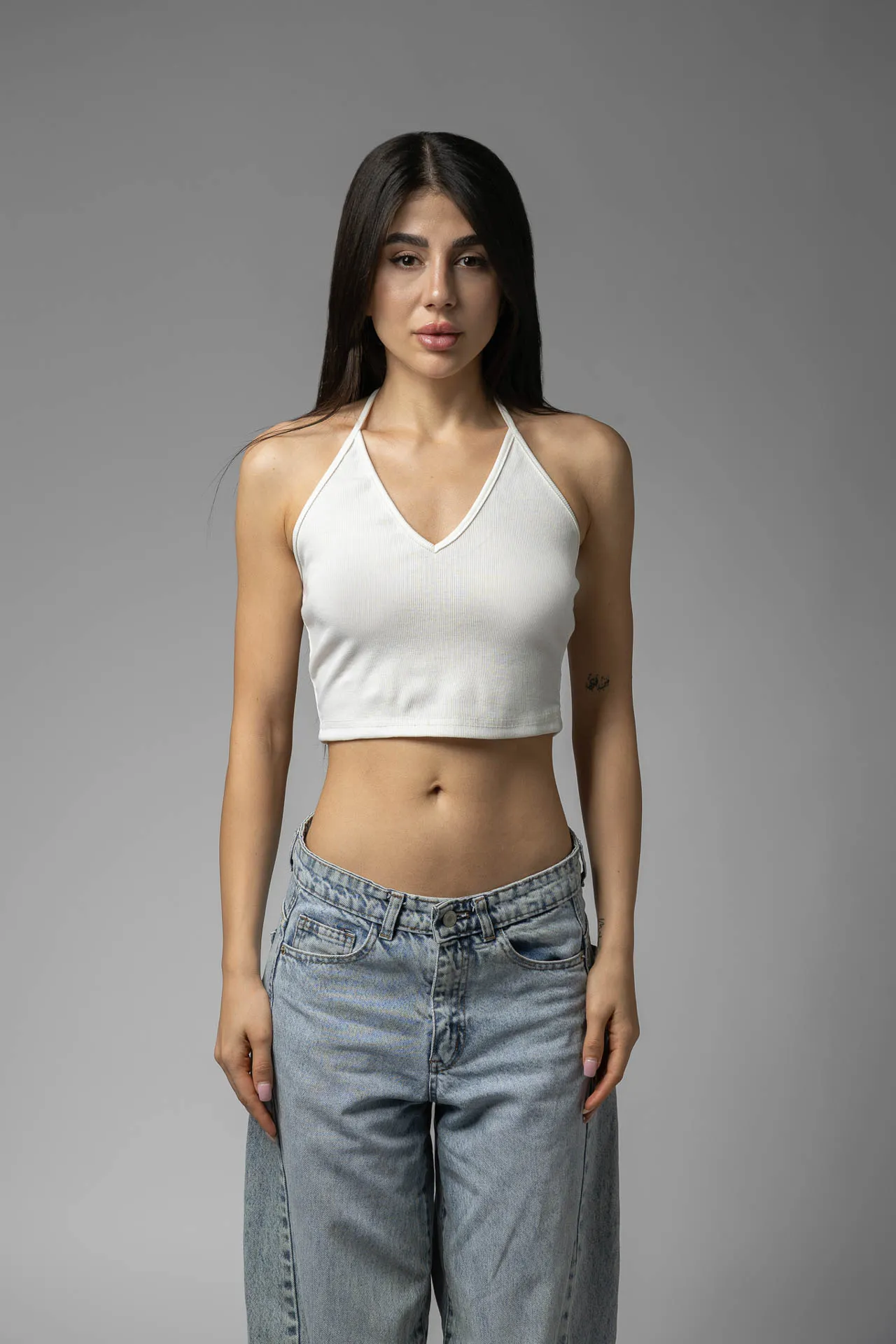 Female model in white halter top and light-wash jeans on gray backdrop — modeling portfolio digitals Dubai