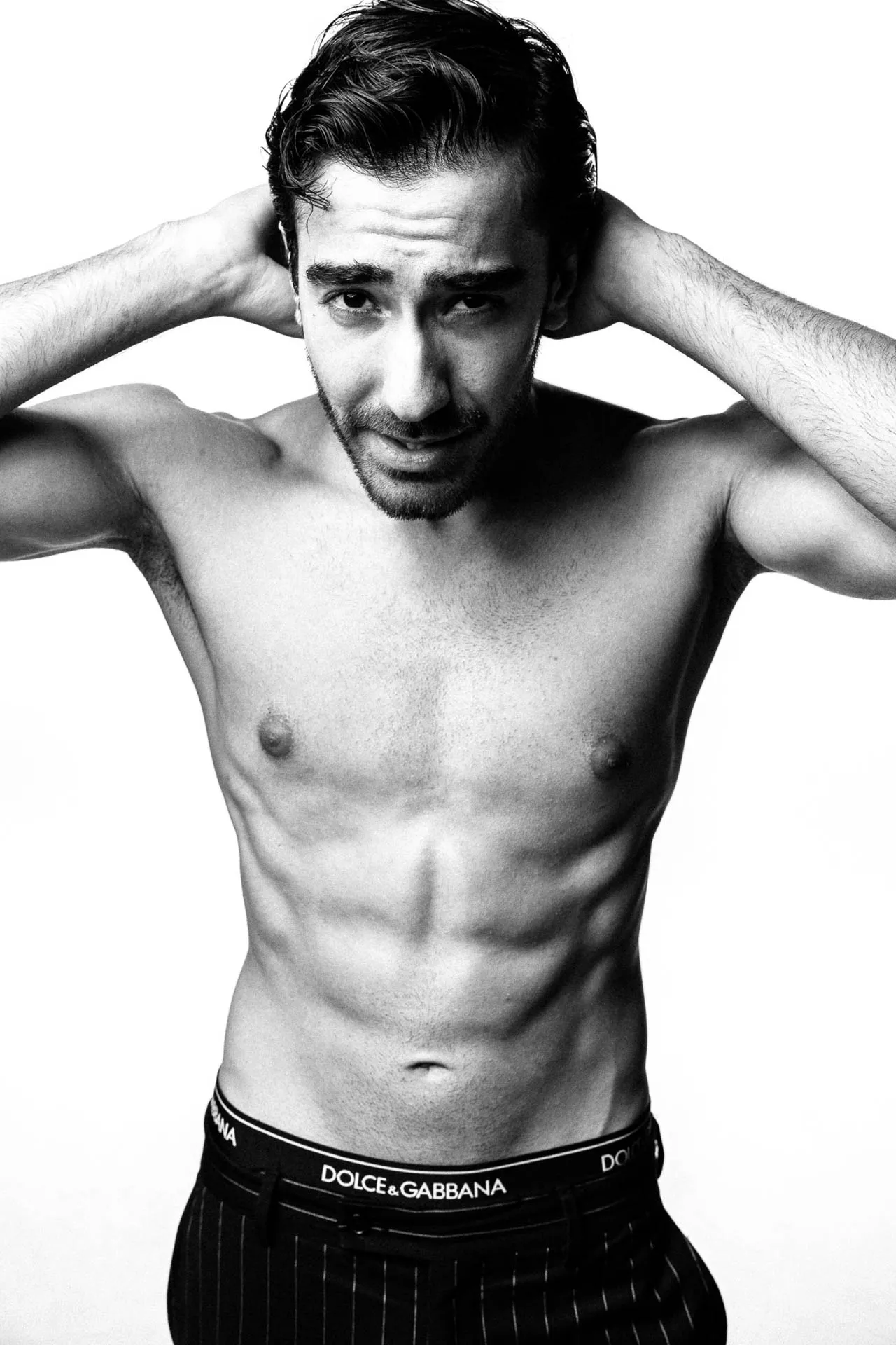 Black-and-white fitness modeling portfolio shot, male model with hands behind head — Dubai studio