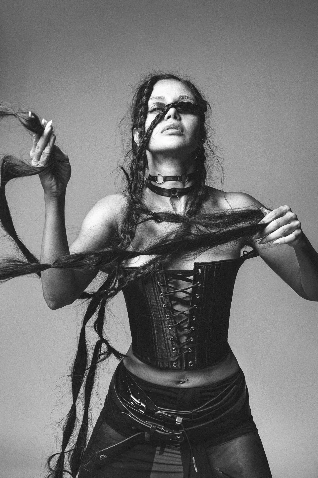 Black-and-white portrait of a woman in a lace-up leather corset, pulling her long hair across her face.