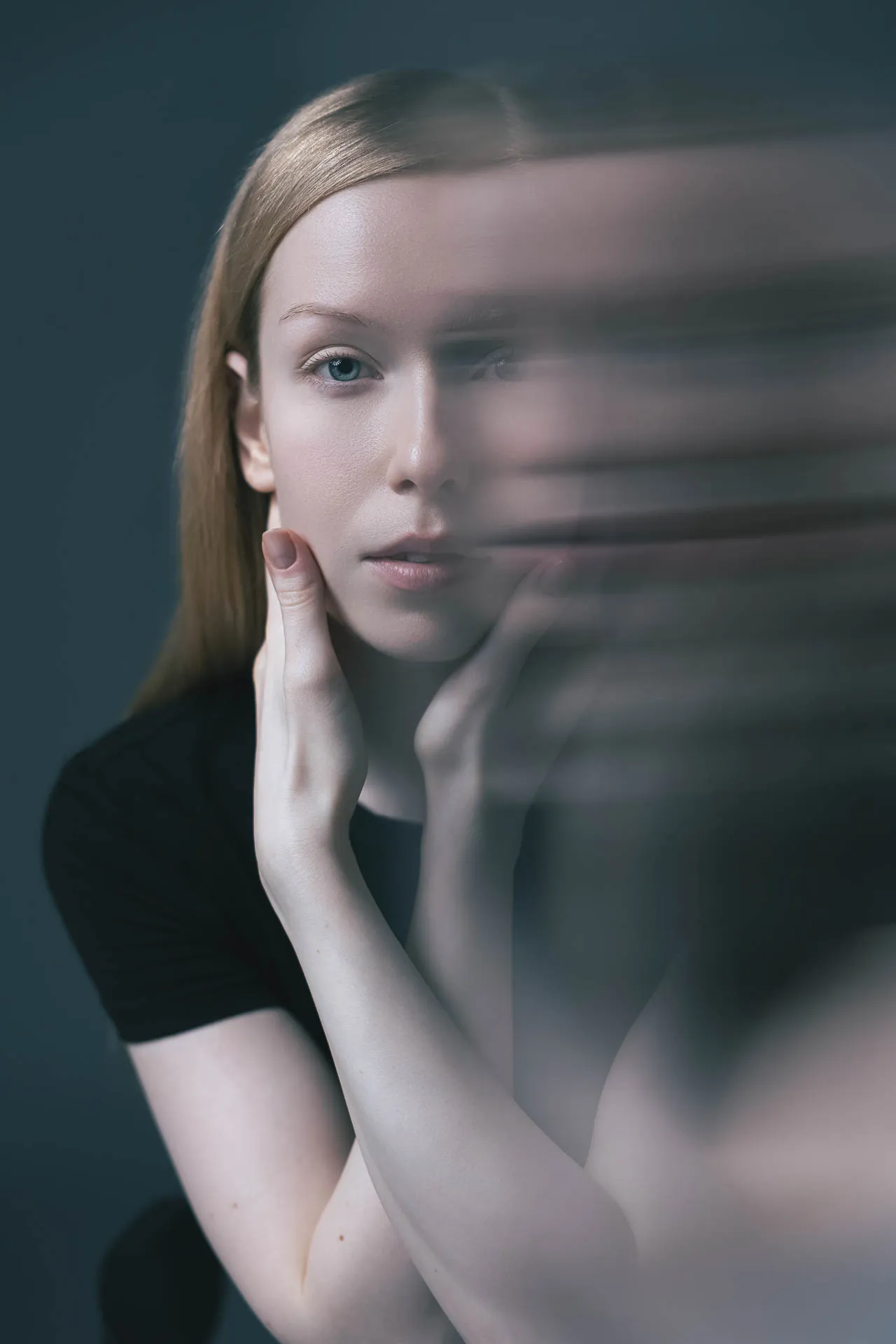 Portrait of a woman looking at the camera with a soft, blurred hand motion across the foreground for an artistic effect.
