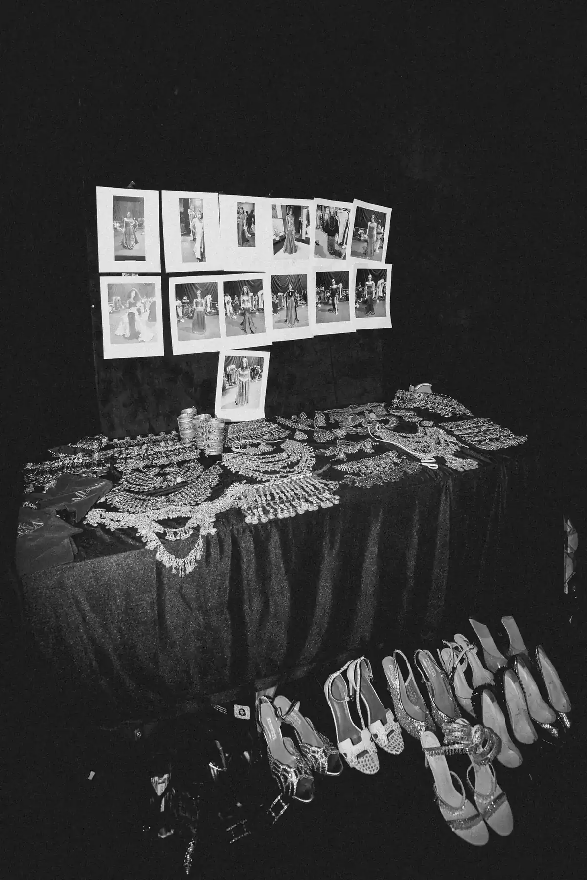 Table covered with jewelry—necklaces, bracelets, and earrings—plus model photos taped to a backdrop behind the display.