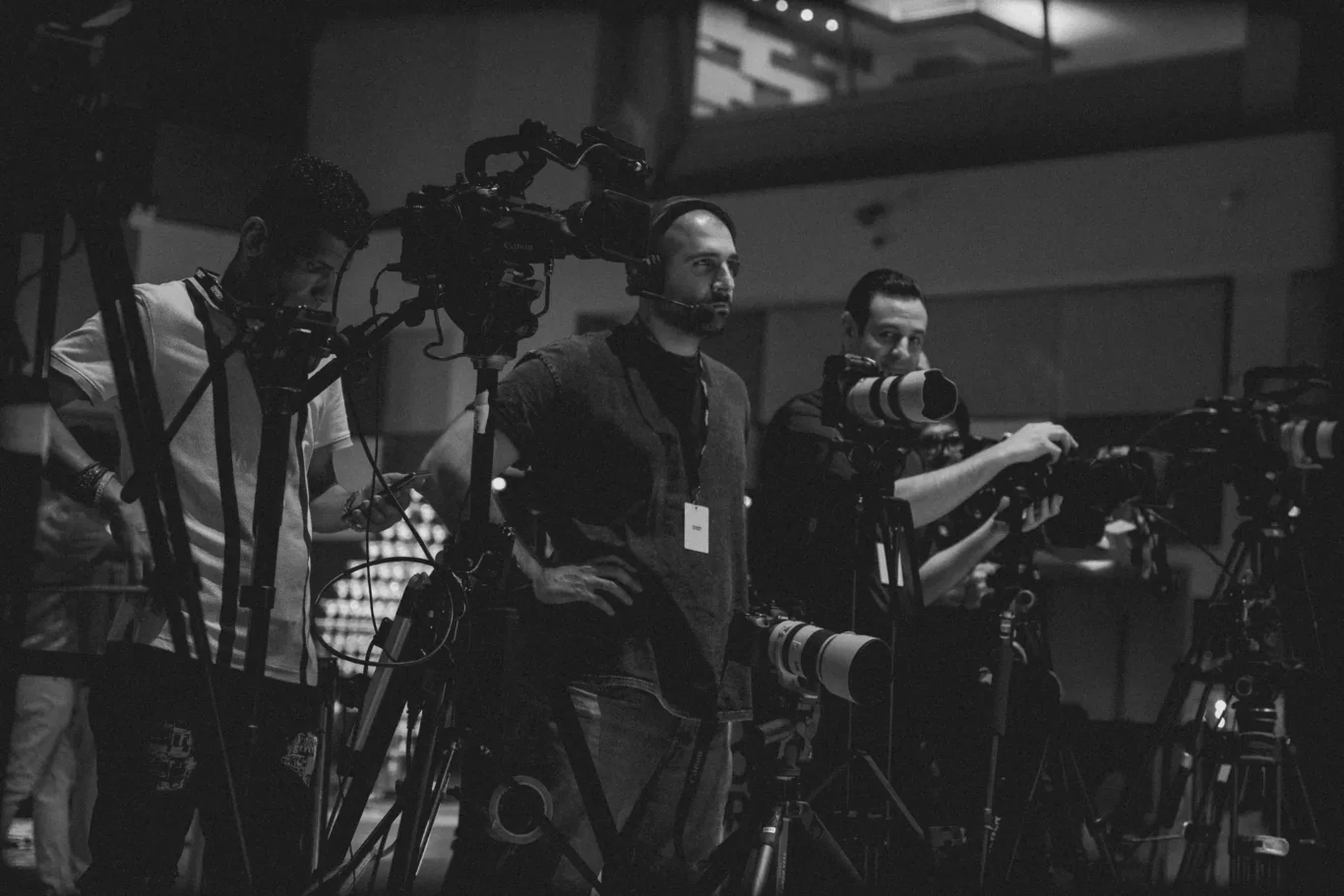 Group of male cameramen with large video cameras on tripods at a film set, monitoring footage.