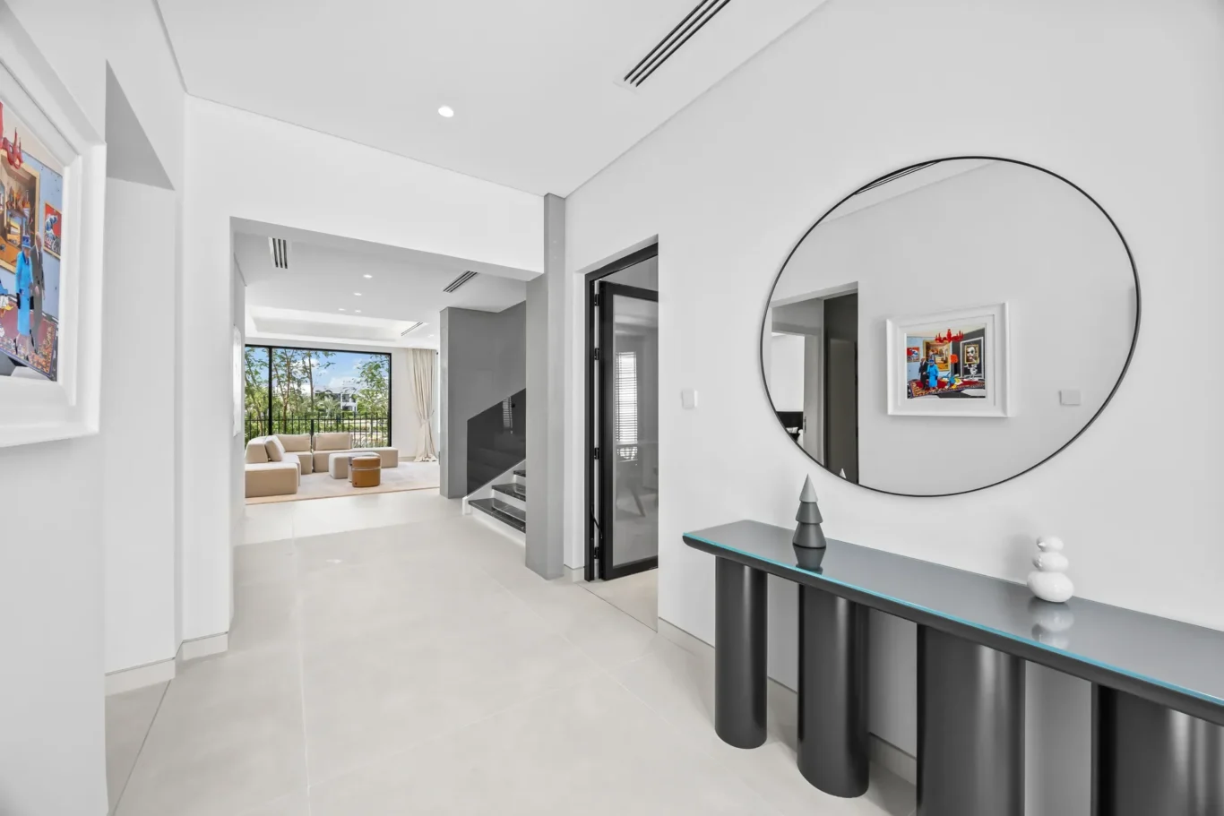 Modern entryway with a large round mirror above a dark glossy console; living room with a beige sofa visible beyond.