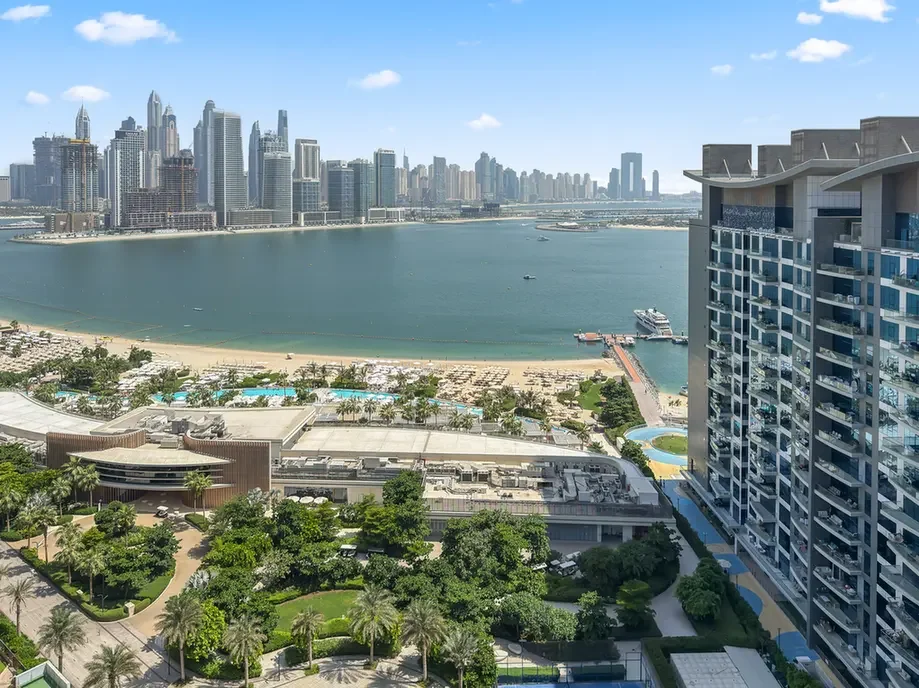 Aerial view of a coastal city: high-rise skyline across a bay with a sandy beach and a tall hotel on the right.