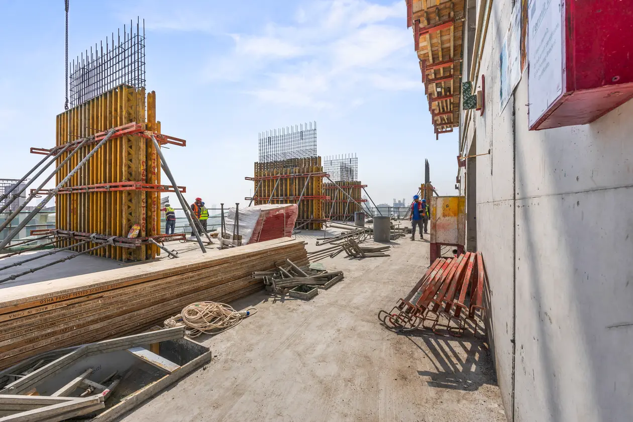 Construction site on a rooftop with workers, wooden formwork, and steel rebar.
