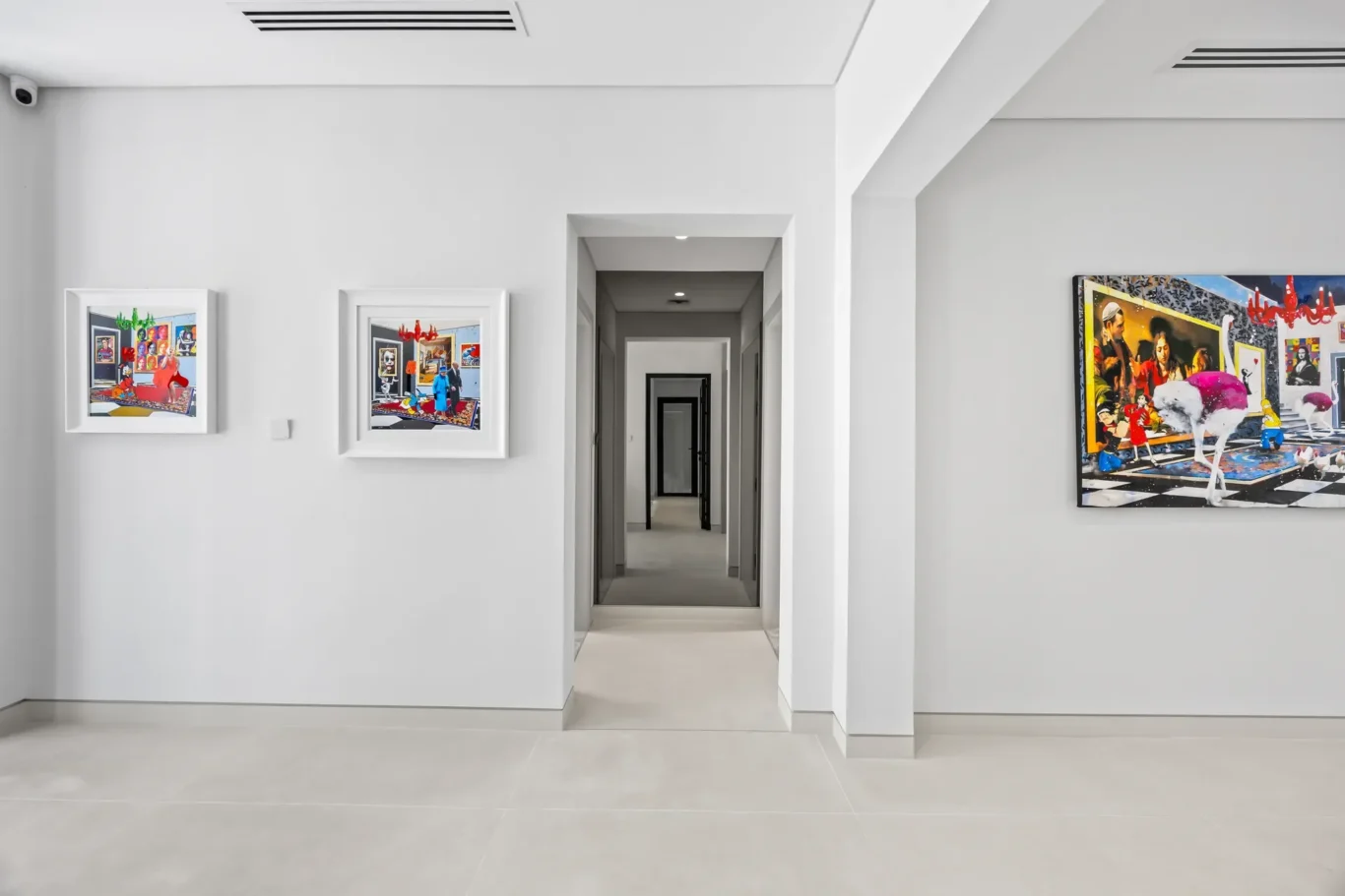 White-walled art gallery hallway with framed colorful paintings on the left and a large mural on the right, receding doorways in the center.
