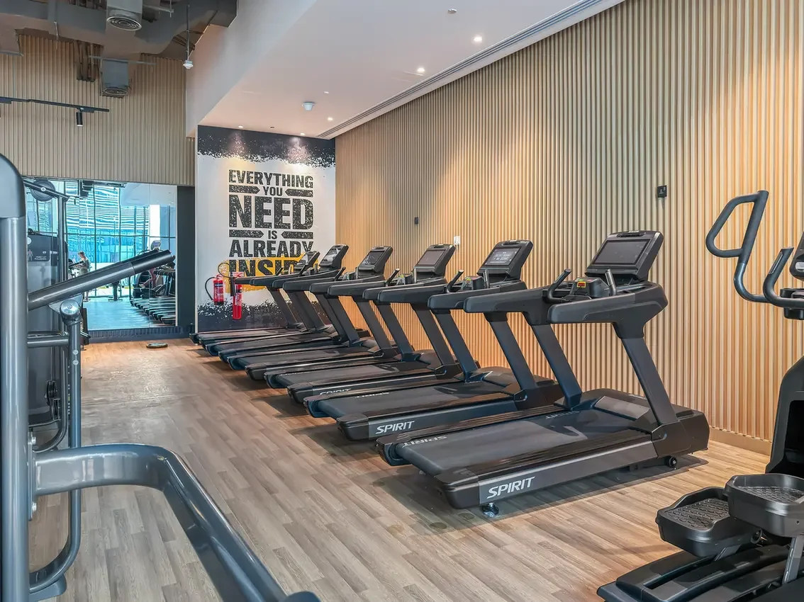 Row of treadmills in a modern gym with wooden wall panels and a motivational quote on the far wall: 'Everything you need is already inside'.