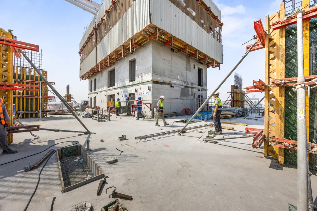 Construction workers in safety vests on a concrete building under construction, with scaffolding and equipment around.
