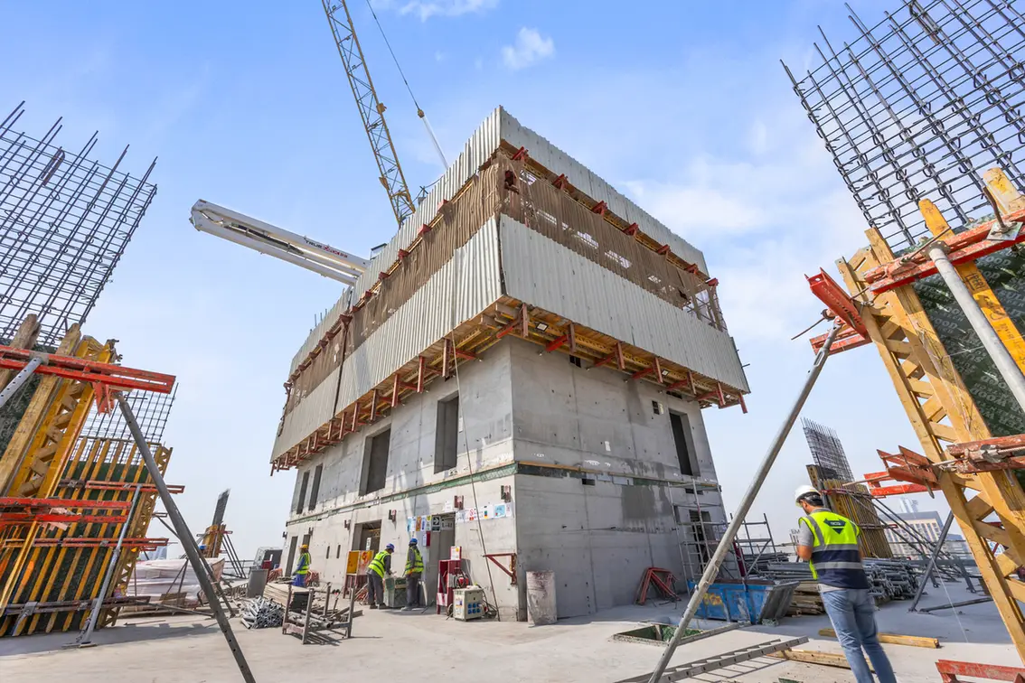 Construction site with a multi-story concrete building under construction, scaffolding, and workers in safety vests and helmets nearby