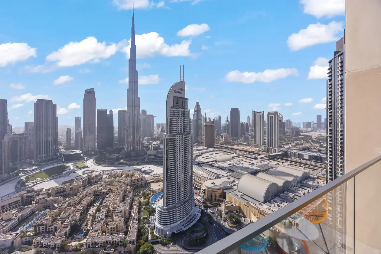 Dubai skyline view from a balcony, featuring tall skyscrapers and a clear blue sky with scattered clouds