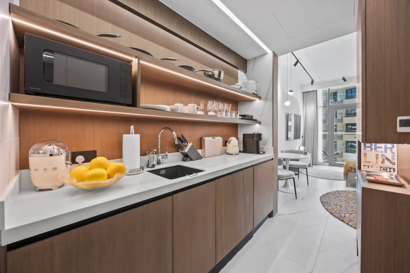 Modern kitchen with warm wood cabinets, white countertop, and microwave on a shelf above the counter.
