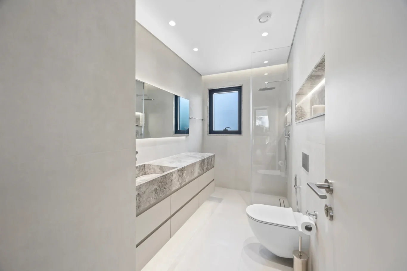 Modern, minimalist bathroom with a marble countertop vanity, large mirror, and glass-enclosed shower. 2. A sleek, gray-and-white bathroom featuring a long marble vanity, wall mirror, and rainfall shower. 3. Contemporary bathroom: double vanity with marble top, frosted window, and a glass shower enclosure. 4. Bright spa-like bathroom with white fixtures, recessed ceiling lights, and a glass-walled shower.