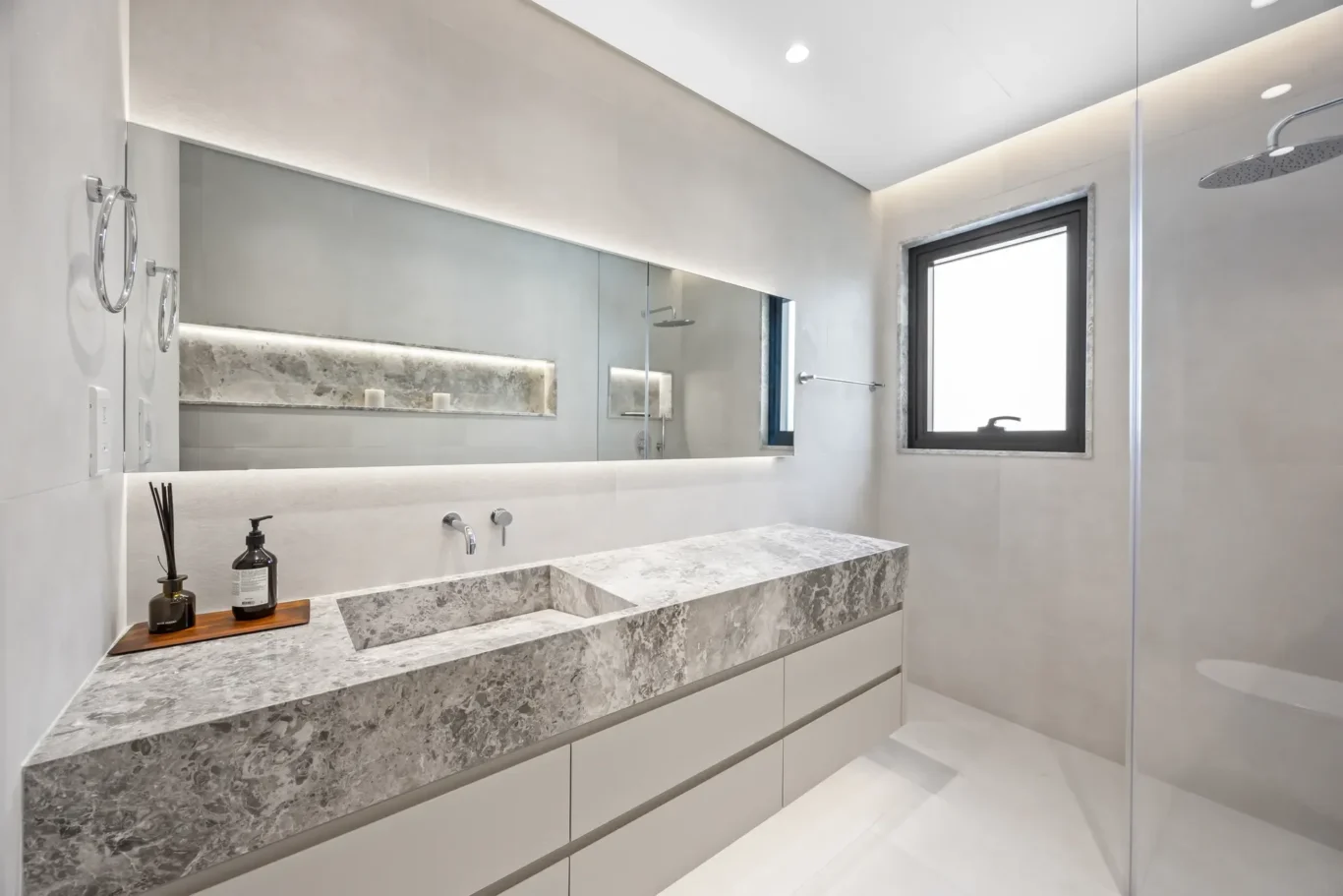 Modern bathroom featuring a long gray marble vanity with integrated sink and wall-mounted faucet, large mirror, and a glass-enclosed shower.