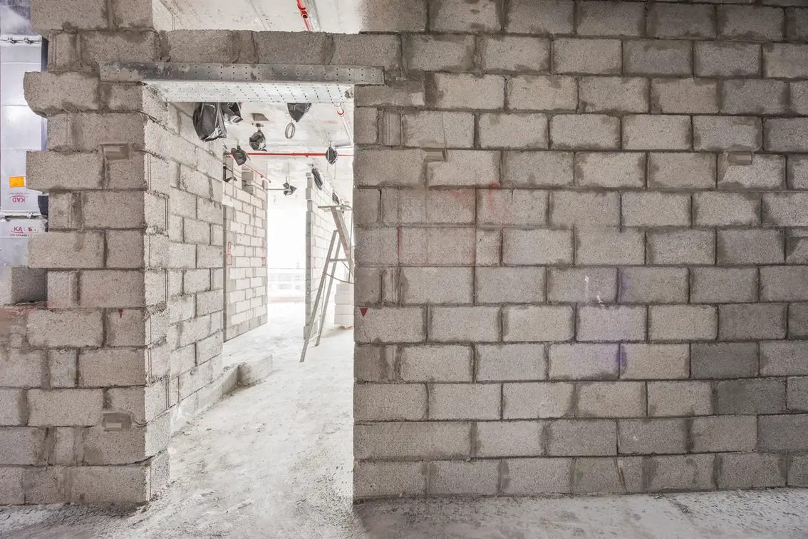 Interior of a building under construction with gray cinder block walls and an arched doorway to a bright hallway.