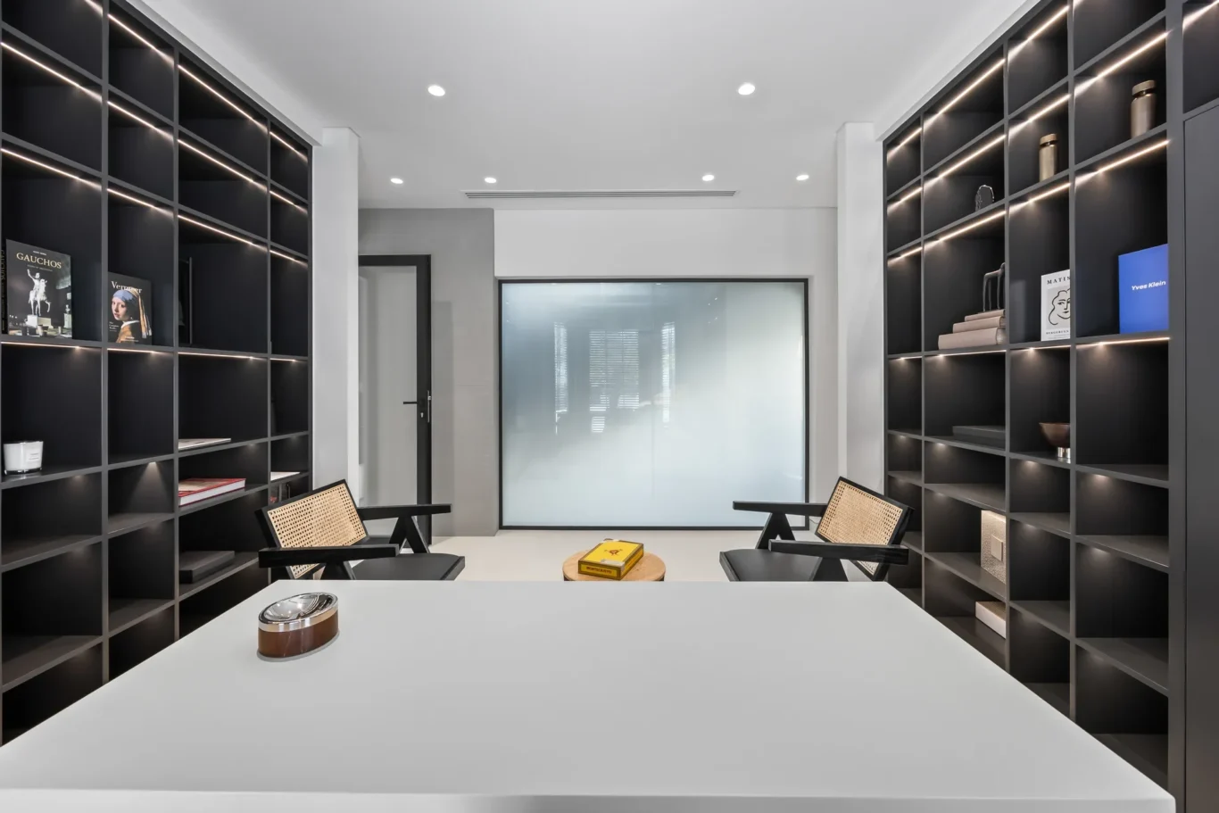 Modern conference room with tall black bookcases along both walls and built-in lighting, facing a frosted glass divider.