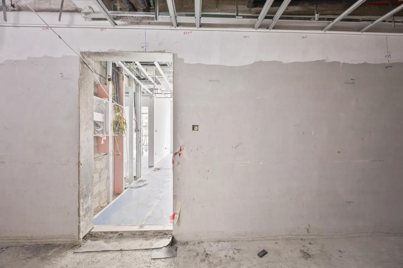 Construction site interior with an open doorway revealing exposed wiring and metal framing beyond the wall border at the edge of a hallway.
