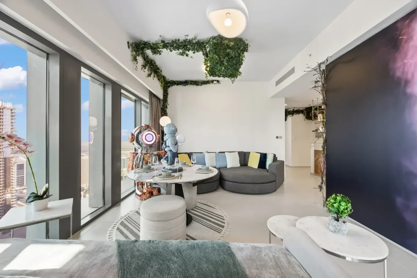 Modern living room with a curved gray sofa, colorful cushions, and large windows overlooking the city.