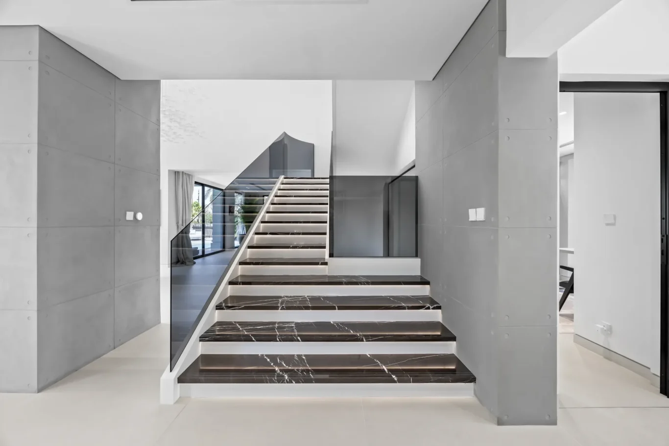 Modern interior staircase with black marble steps and a glass balustrade in a white-gray hallway at a contemporary home.