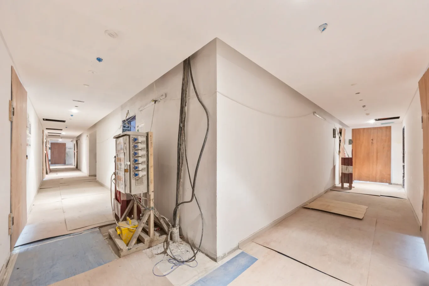 Construction hallway under renovation with exposed cables and scattered debris along the floor central partition in progress
