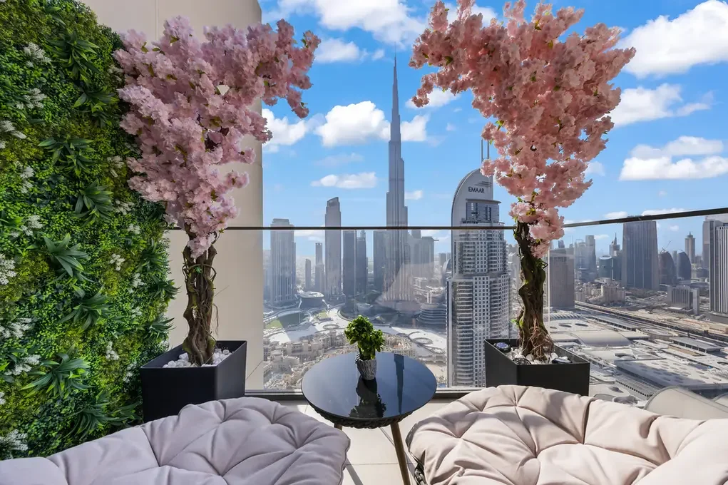 Rooftop terrace with pink flowering trees in pots, a glass railing, and a distant city skyline.