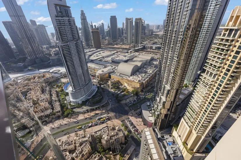 Aerial view of a dense modern city with numerous skyscrapers, busy streets, and a large shopping complex at street level.