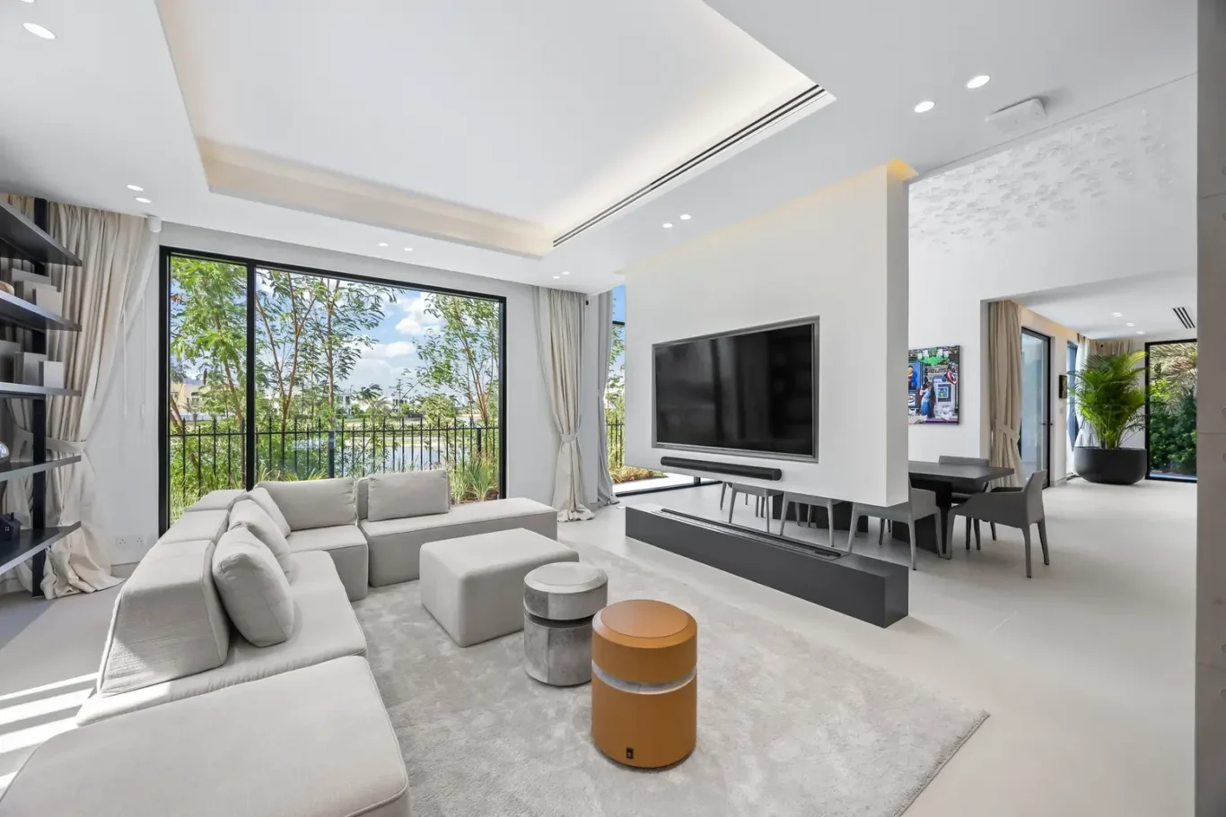 Bright open-concept living room with large glass doors to a garden, a gray sectional sofa, and a wall-mounted TV