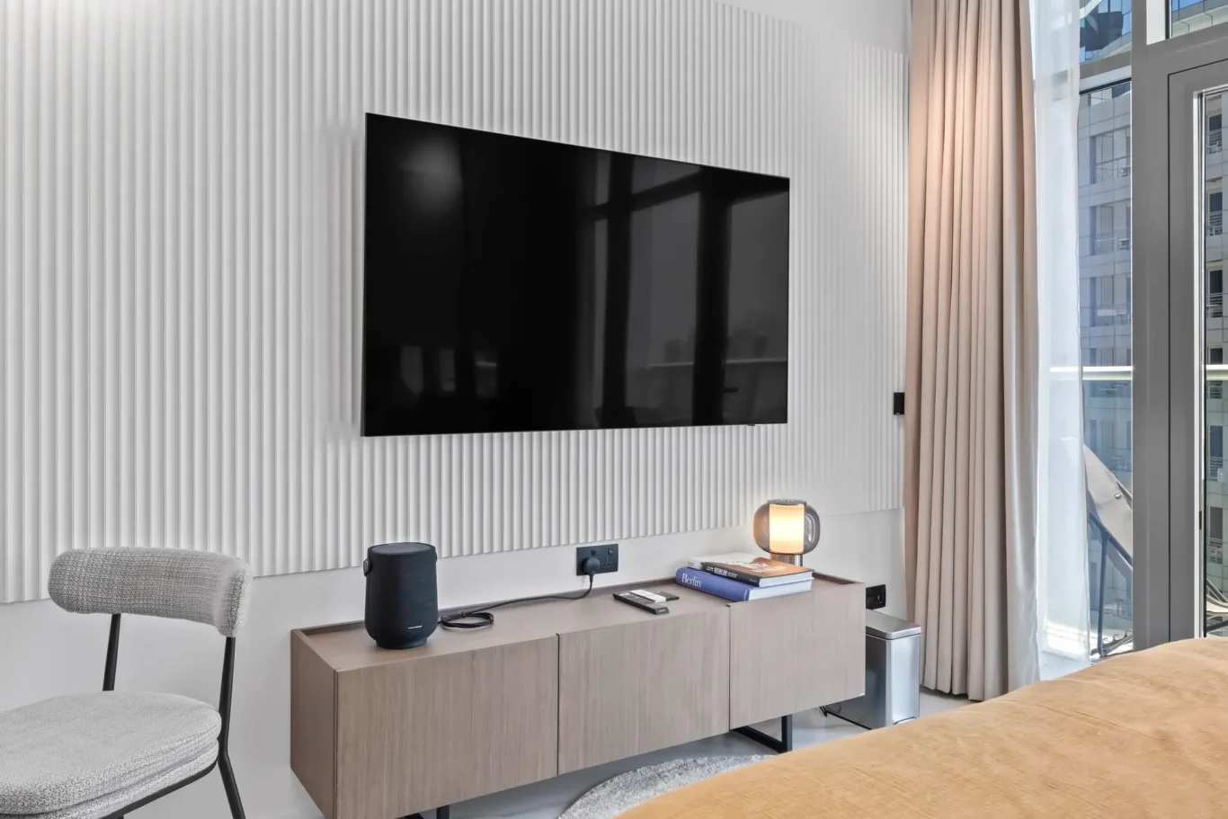 Wall-mounted flat-screen TV on a textured, vertical-panel wall above a wooden cabinet in a modern living room.