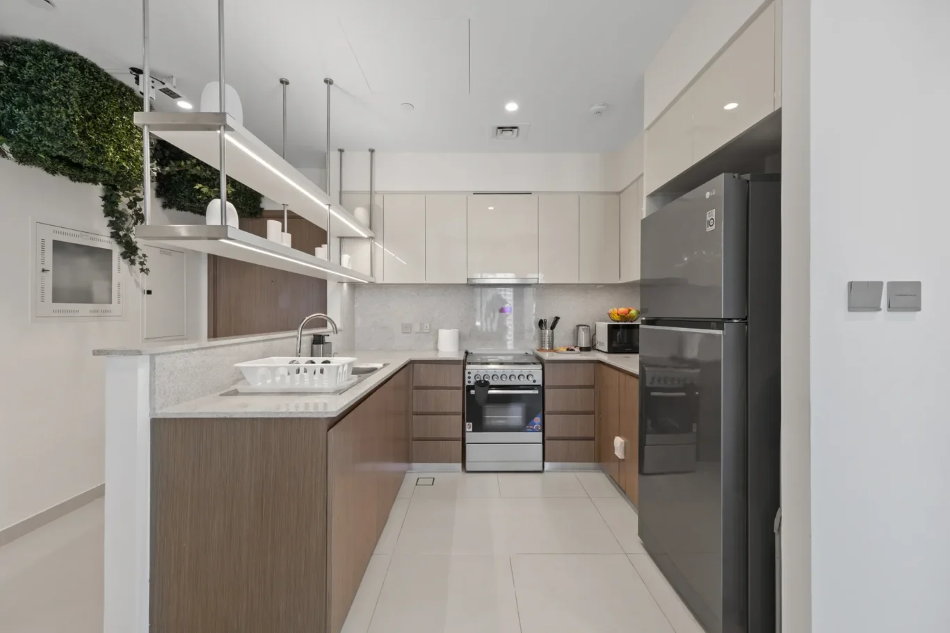 Bright modern kitchen with white upper cabinets, wood lower cabinets, and a green plant wall along the left side.