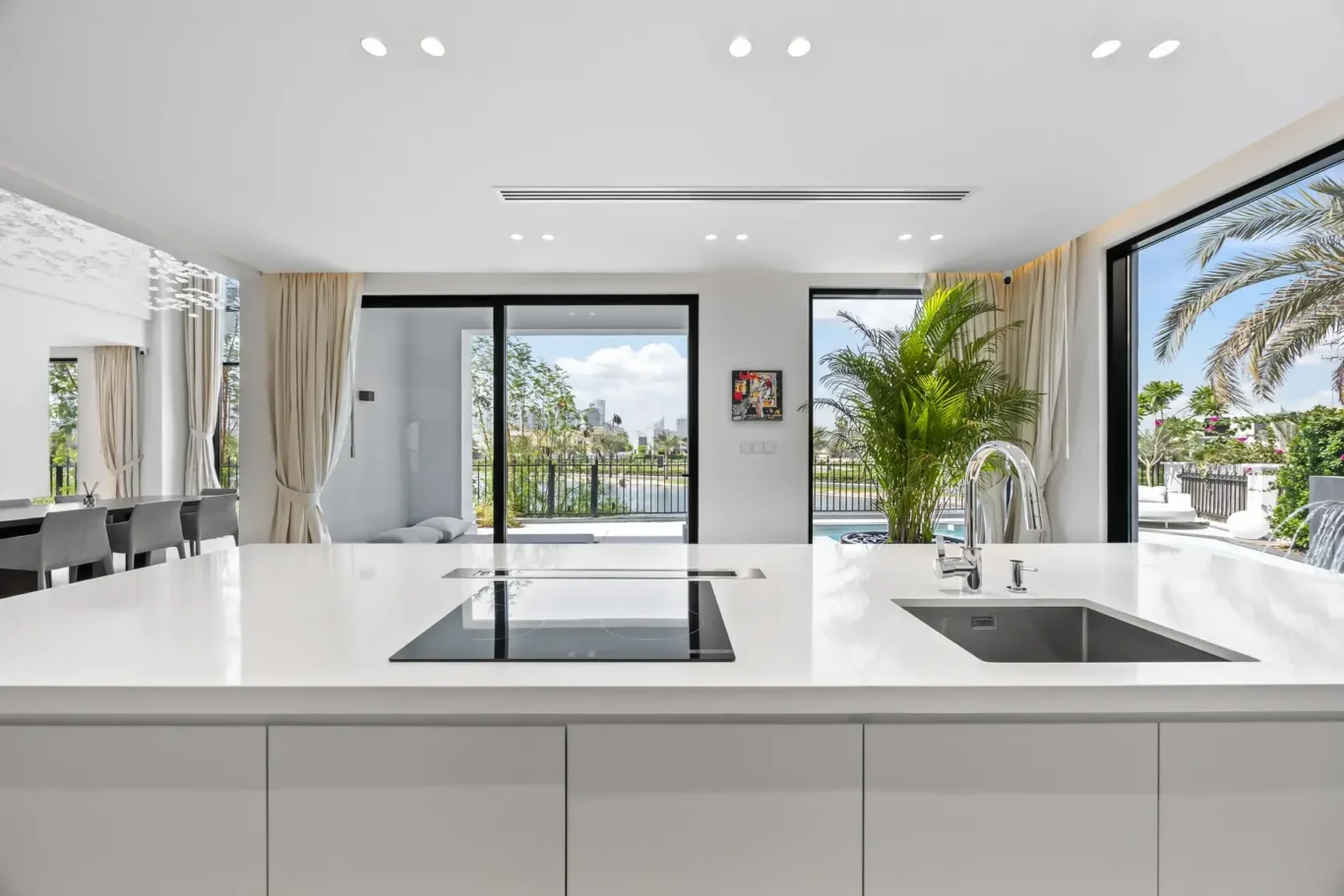 Bright, modern kitchen with white island, integrated induction cooktop, and a double-bowl sink; large glass doors open to a sunny outdoor space.