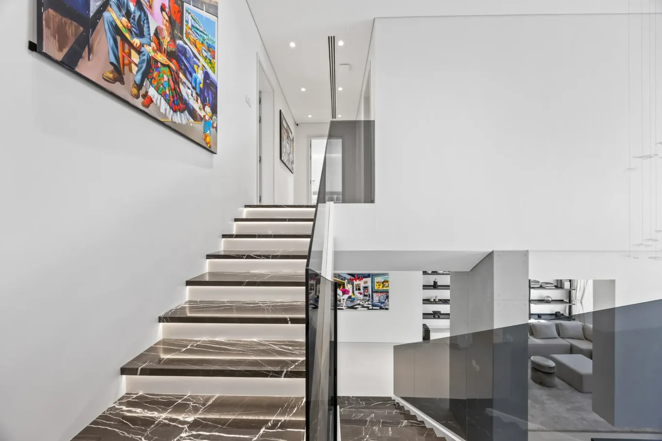 Modern two-story interior with dark marble stairs and glass railing, white walls, and colorful artwork along the stairwell