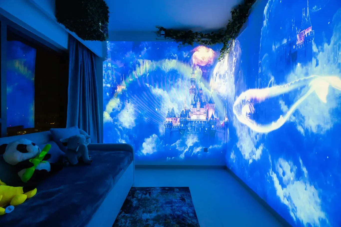 Cozy kids' room with a blue castle projection wrapping around the walls and a sofa with plush toys on it.