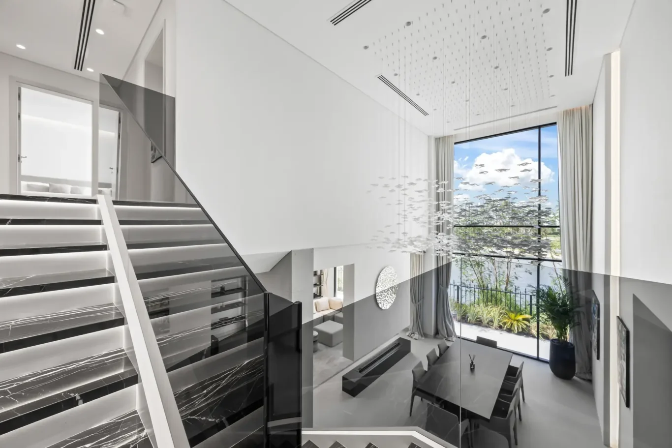 Modern two-story foyer with black marble staircase, glass railing, and a large window overlooking a garden.