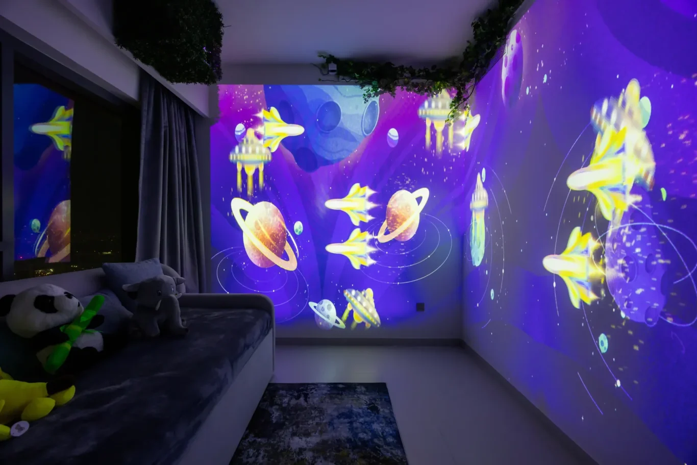 Cosy kids' bedroom with a sofa bed and plush toys, illuminated by a purple space-themed wall projection featuring planets and rockets.