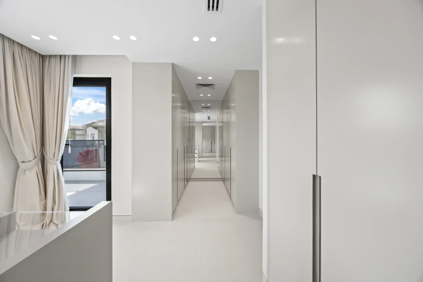 Long bright hallway with glossy gray lockers on both sides and a window with beige curtains on the left.