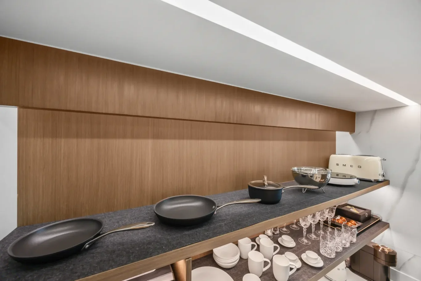 Modern kitchen display with wood panels, dark countertop, pans, and a SMEG toaster on the right.