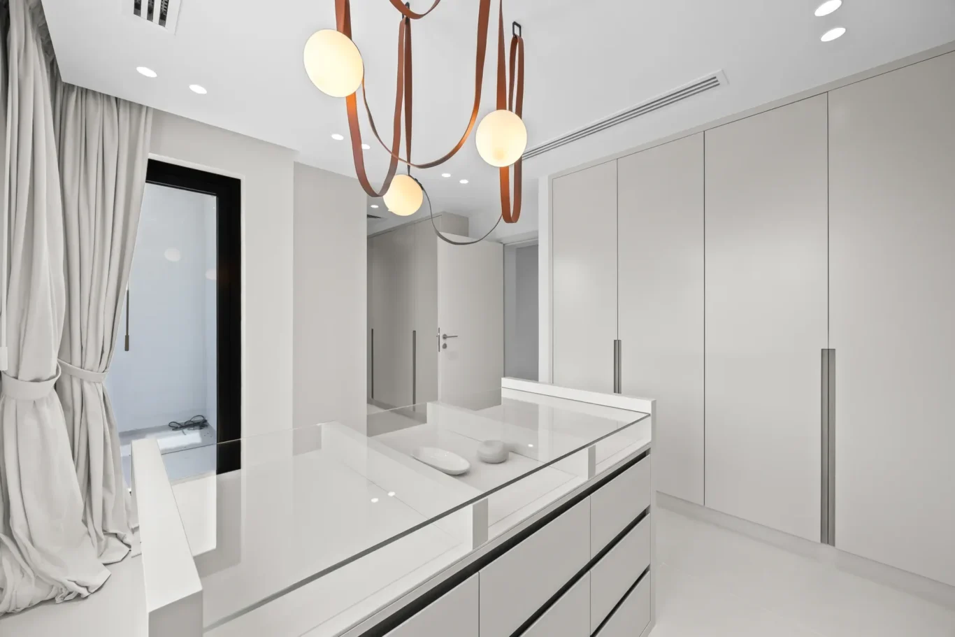 Modern white kitchen with glossy cabinets, a glass-tinish island, and brown leather-strapped pendant lights overhead.