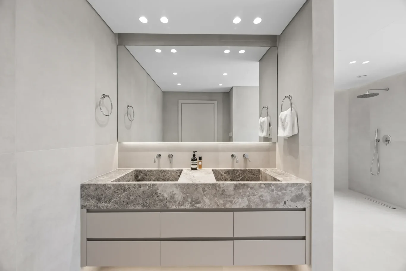 Modern bathroom with gray double vanity, marble countertop, and large rectangular mirror reflecting recessed lighting and a doorway behind the sink area