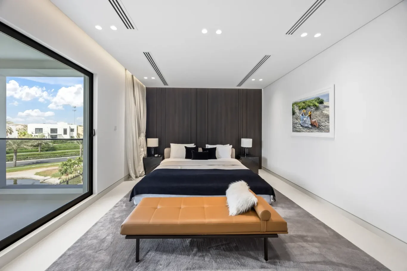 Modern bedroom with a large floor-to-ceiling window showing a sunny outdoor view; central bed with neutral bedding and dark wood headboard flanked by black nightstands.