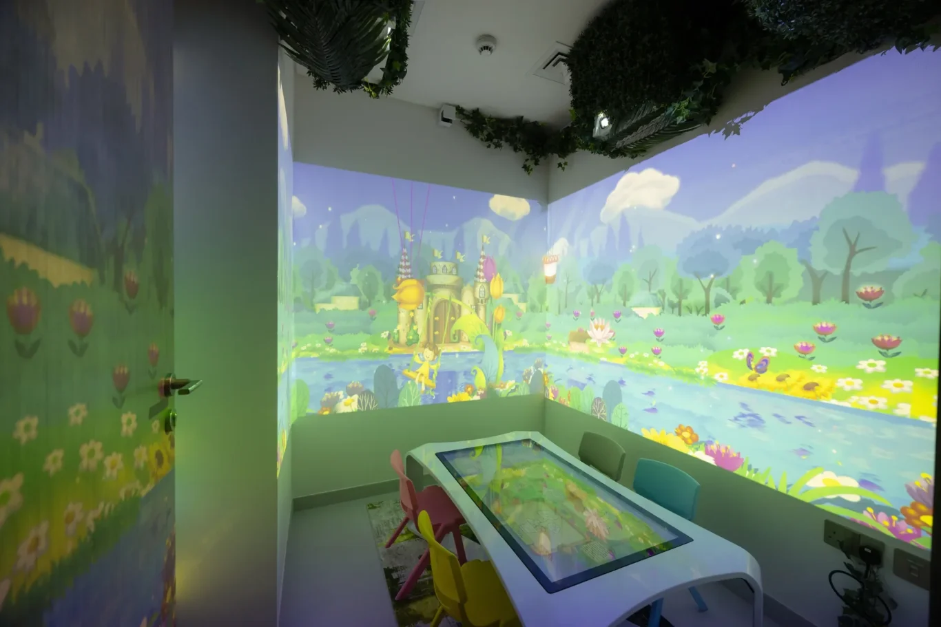 Vibrant fantasy garden mural encircles a children's play table with a touchscreen surface.