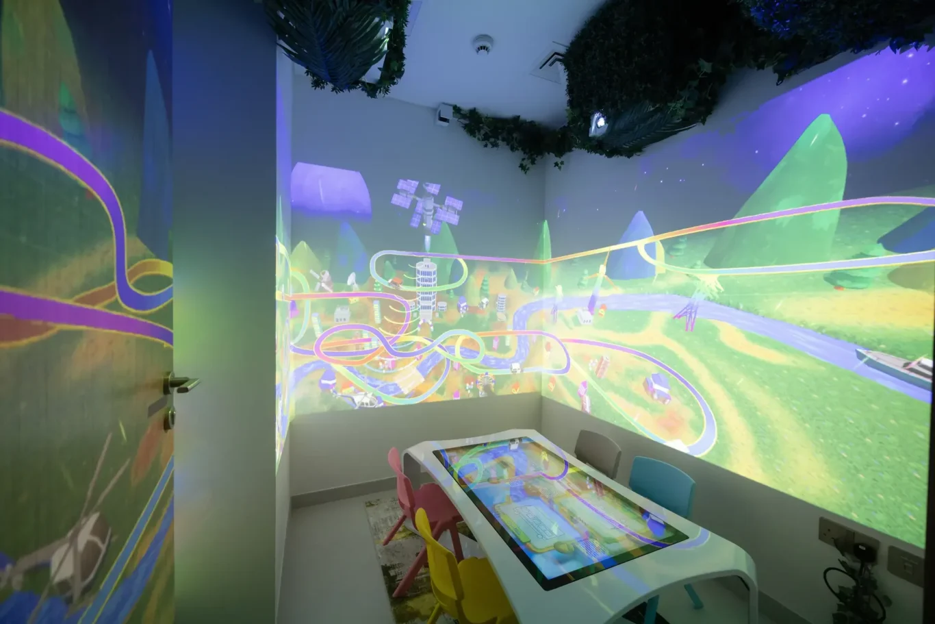 Colorful children’s play room with a touchscreen game table and bright mural of a roller-coaster and mountains.