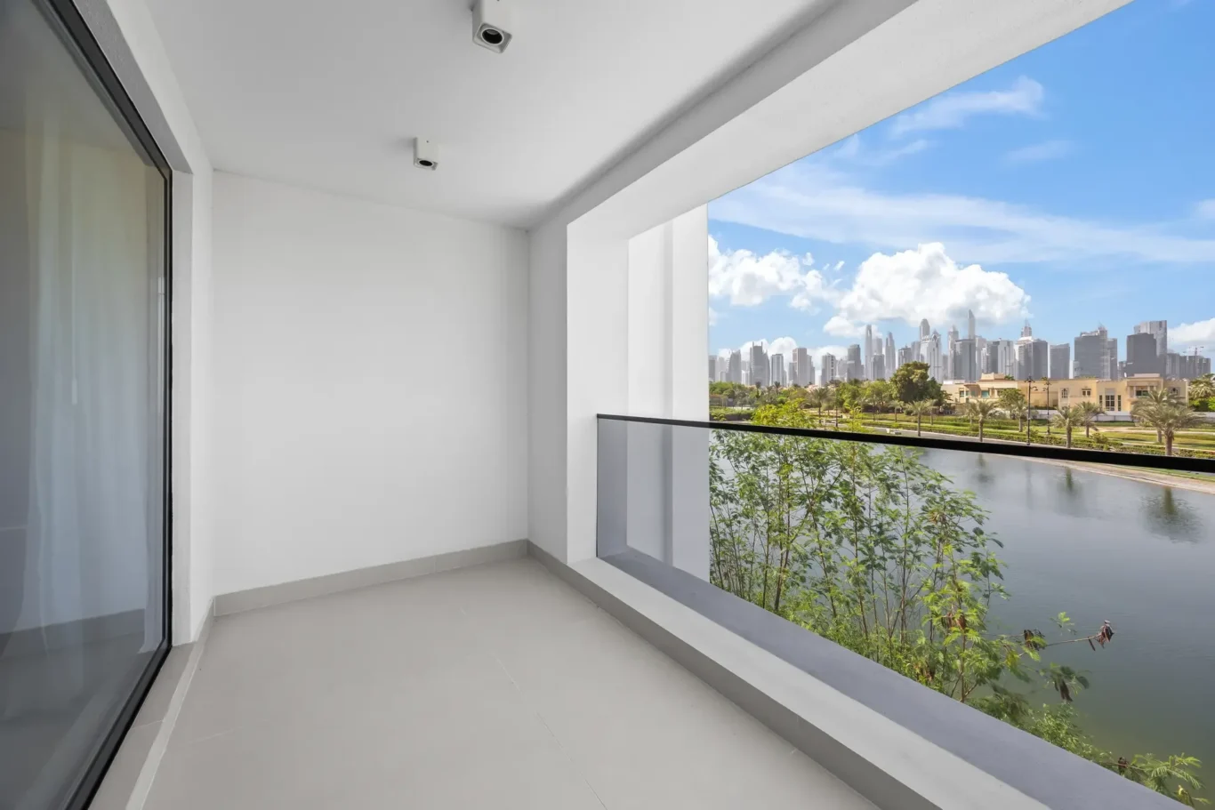Balcony with glass railing overlooking a waterway and distant city skyline on a sunny day.