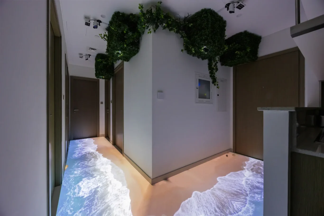 Indoor hallway with closed doors and hanging greenery; the floor is lit with an ocean wave projection.