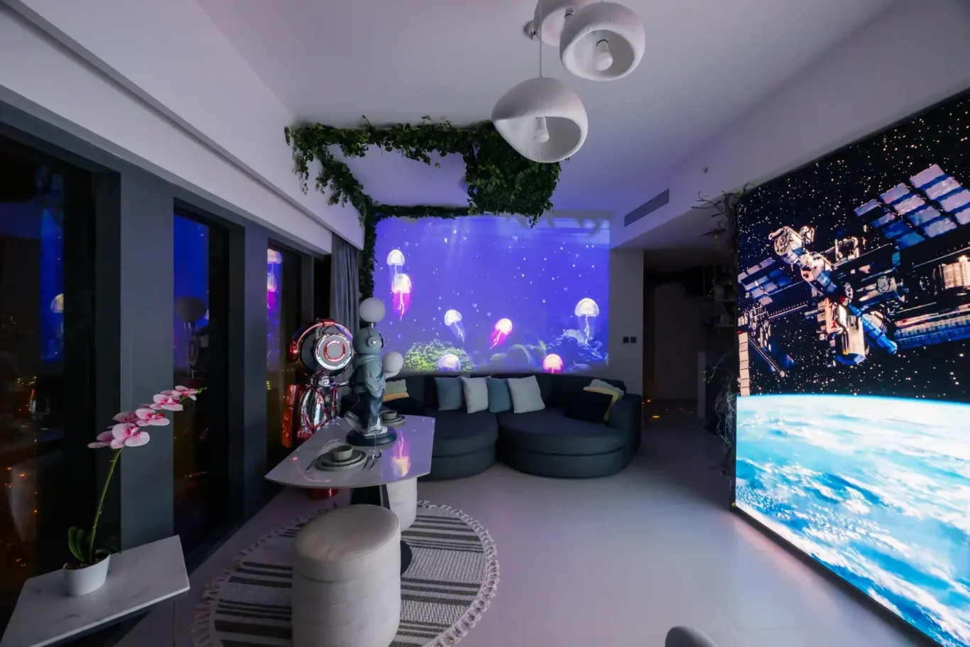 Living room with a blue underwater jellyfish projection on the wall, green ivy decor, and a gray circular sofa setup.
