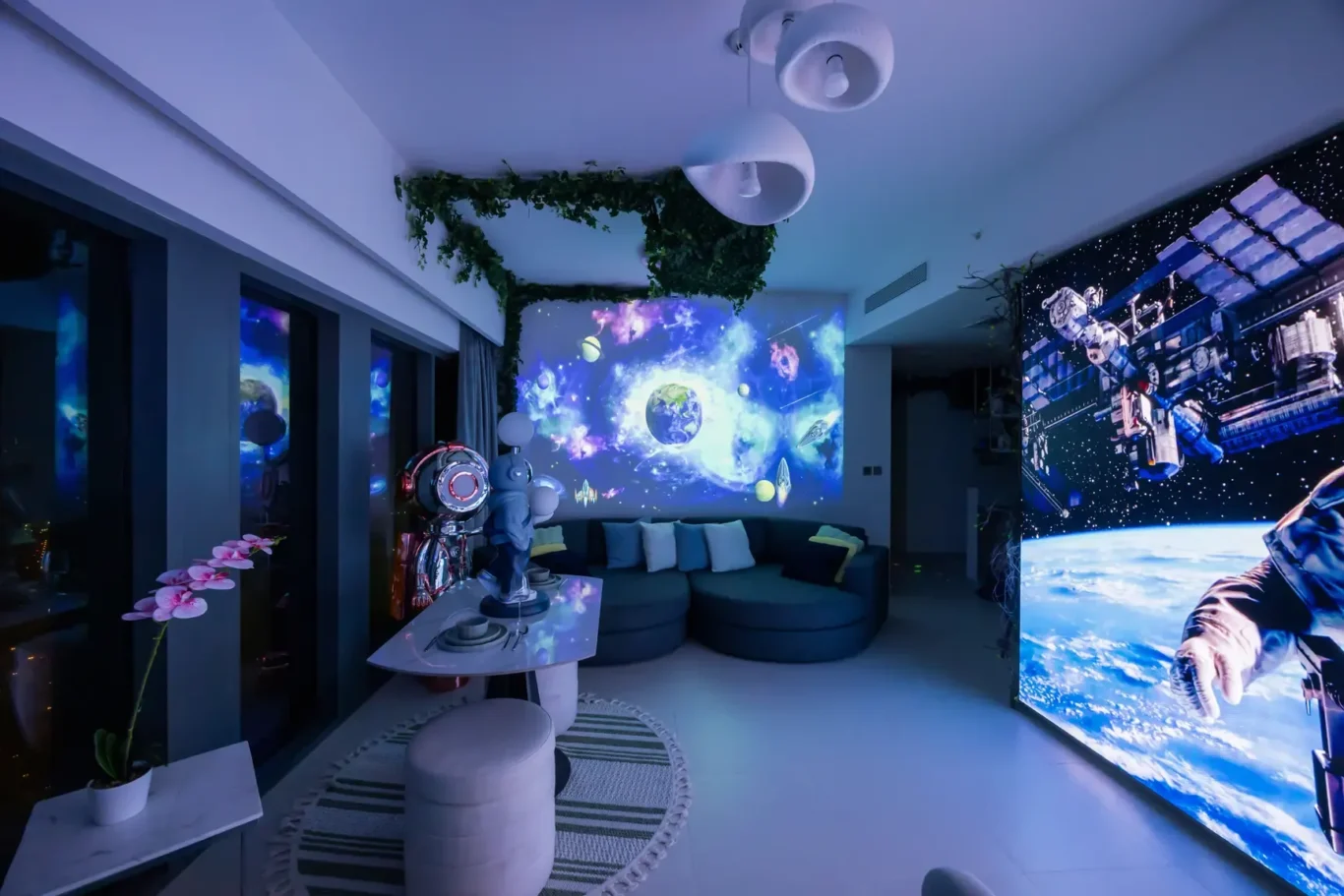 Living room with a wall-scale space projection of Earth and planets, blue lighting, and a curved couch in the center.