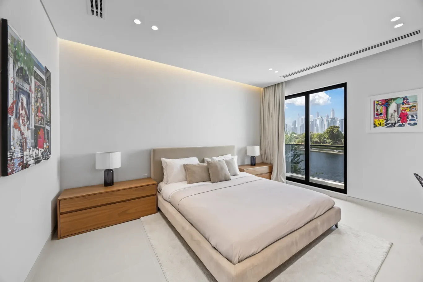 Modern bedroom with a low beige bed, two wooden nightstands, and black lamps; large window with city skyline view.