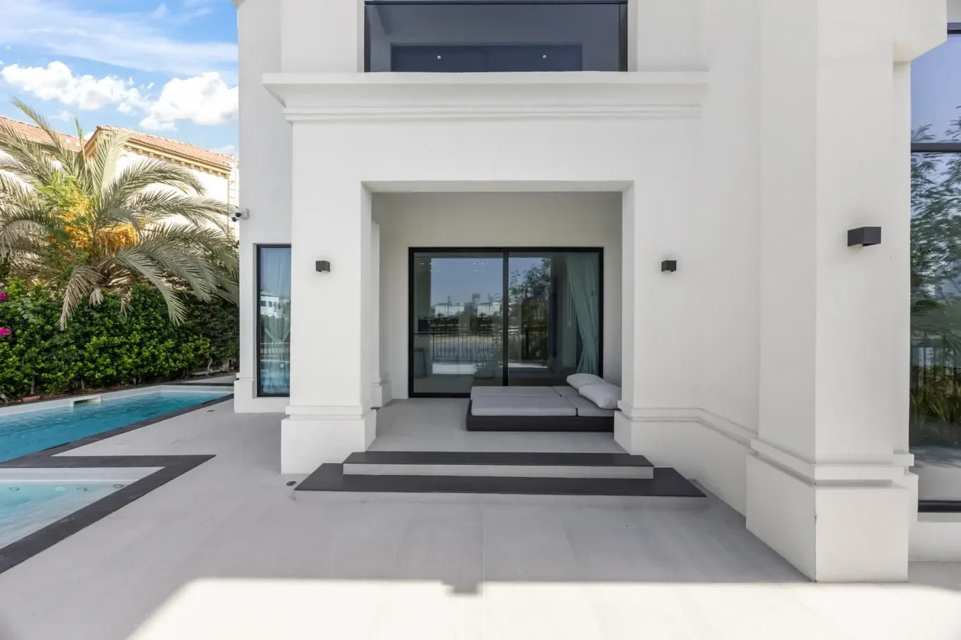 Modern white villa with a shaded patio, black-framed glass doors, and a poolside seating area.